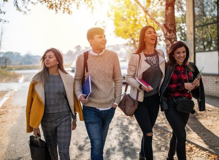 young adults walk along a sunlit path, smiling and laughing